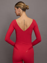 Model wears a long sleeve, deep v neck top in bright red with an overlapping seam at the bottom creating the effect of a wrap top. 