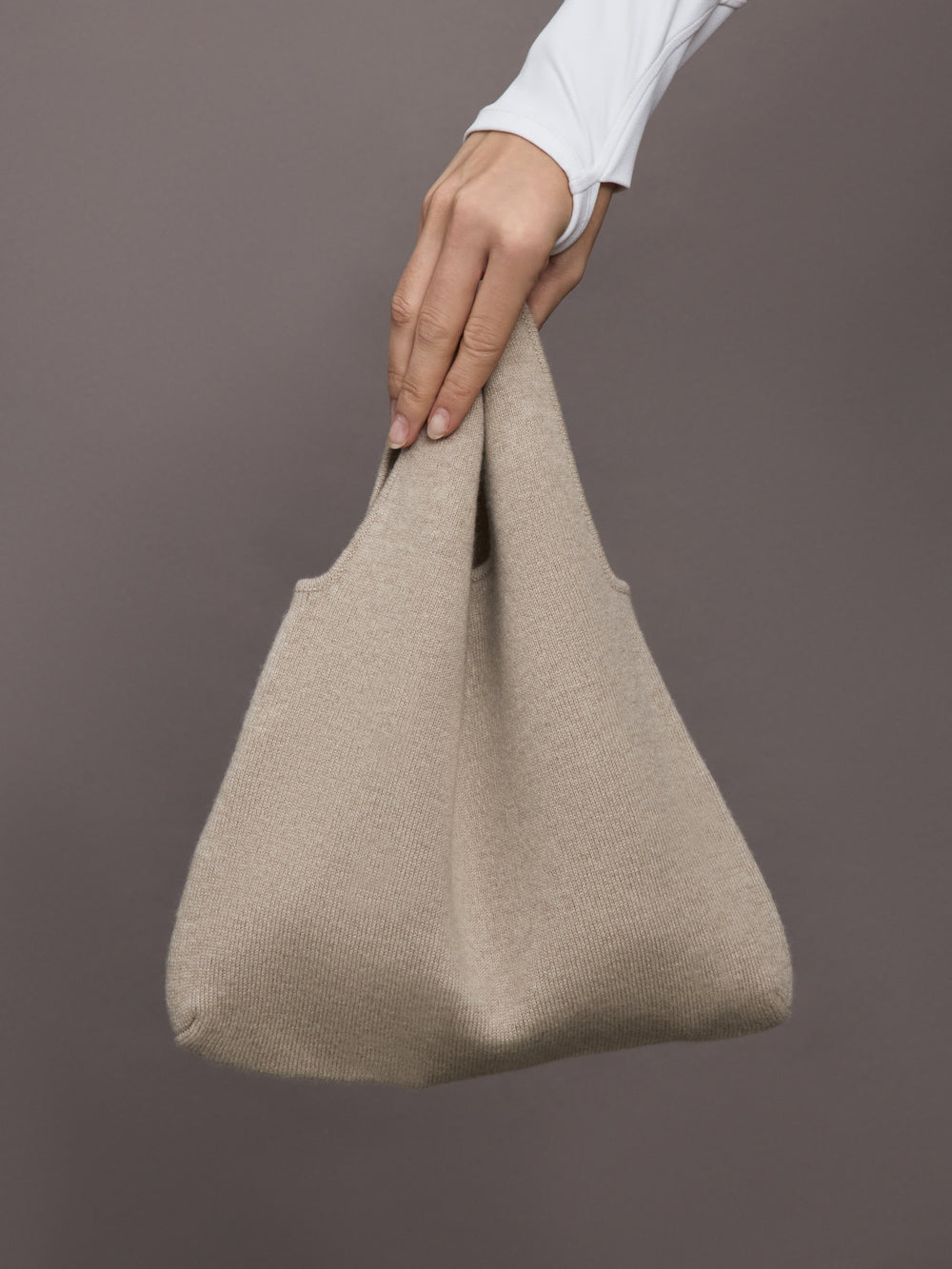 Model wears a double handled taupe linen textured bag on her arm.