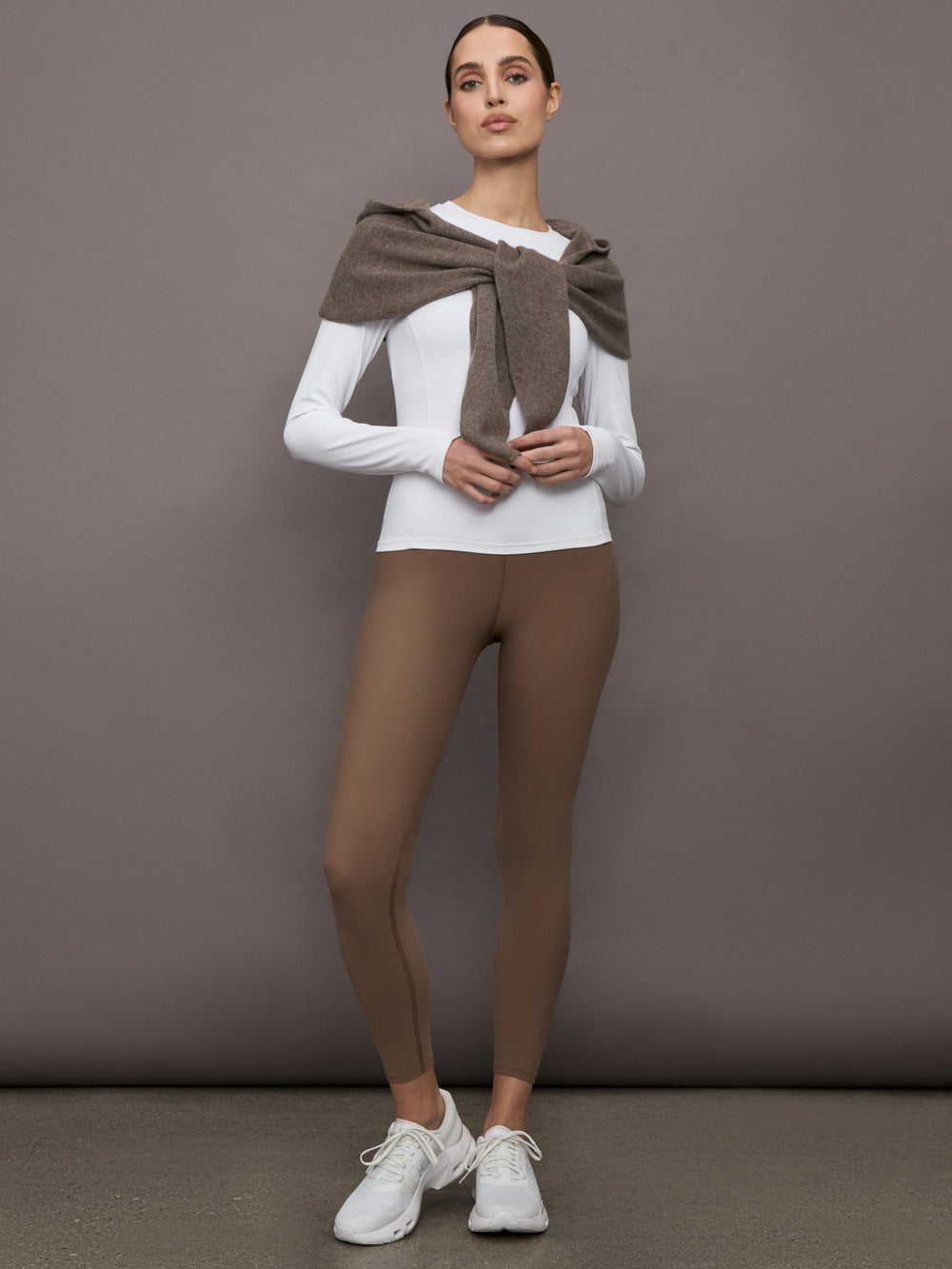 Model wears a muted brown colored hooded scarf over her shoulders. 