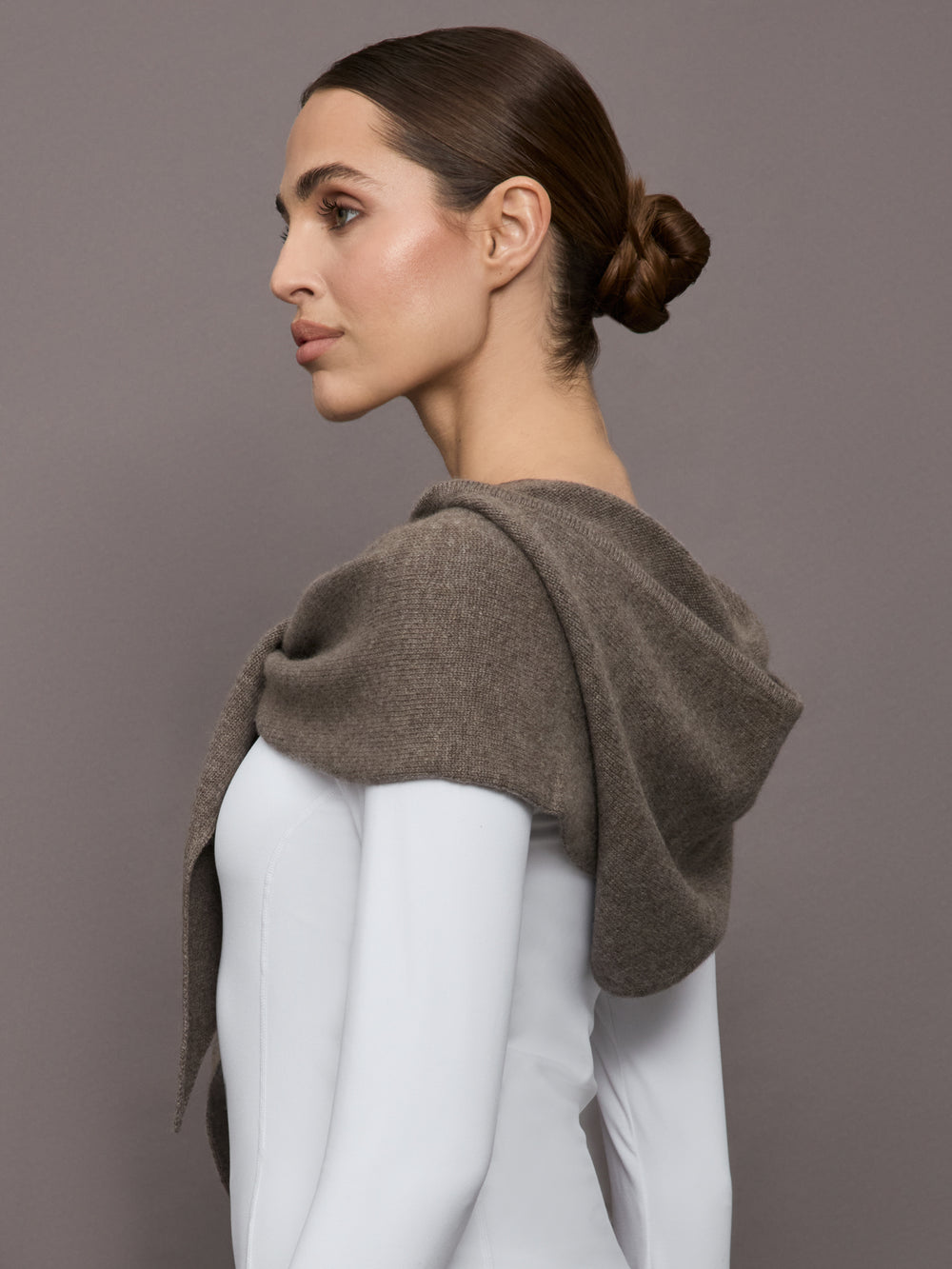 Model wears a muted brown colored hooded scarf over her shoulders. 