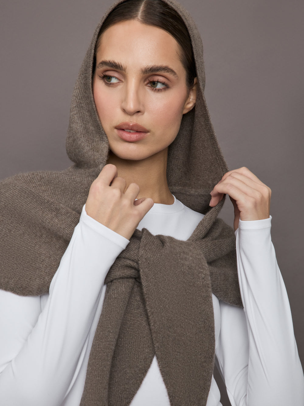 Model wears a muted brown colored hooded scarf over her shoulders. 